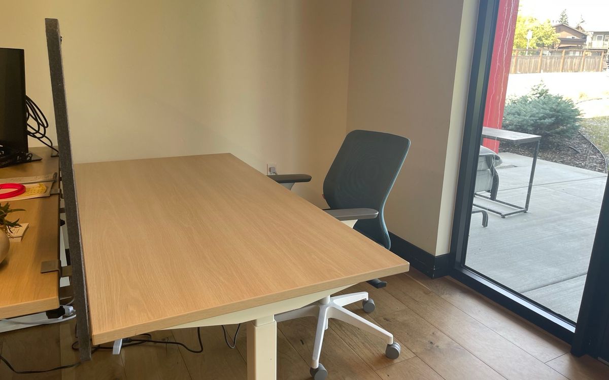 A dedicated desk beside the full-height windows on the downstairs floor, with a sit-stand top and task chair