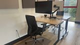 The same dedicated desk from the side, showing the sit-stand frame and floor mat