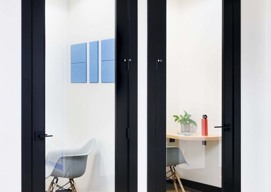 Glass-doored phone booth with a small desk and chair