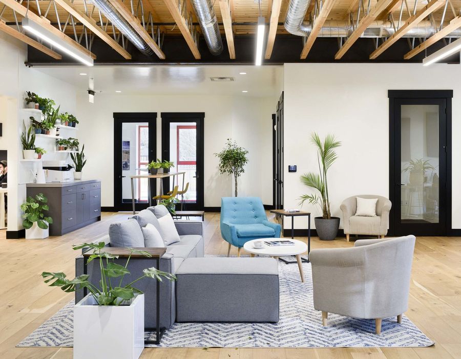 Open lounge with exposed glulam beams, armchairs, and plants